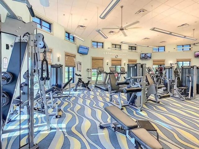 exercise room with carpet floors, ceiling fan, and a towering ceiling