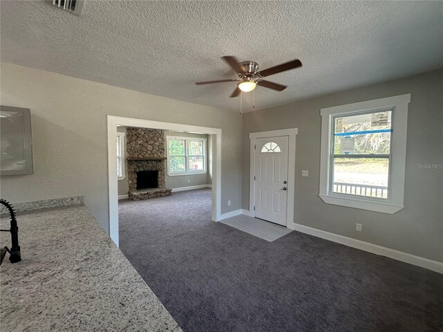 carpeted foyer entrance with ceiling fan, a textured ceiling, and a fireplace