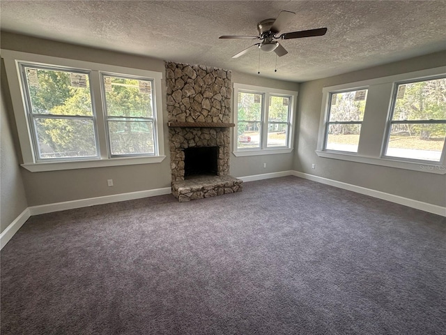 unfurnished living room featuring a textured ceiling, ceiling fan, a stone fireplace, and dark colored carpet