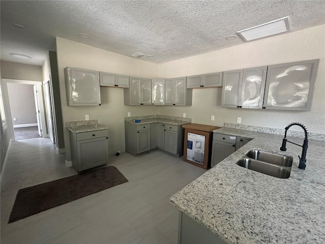 kitchen featuring gray cabinetry, a textured ceiling, light stone counters, and sink