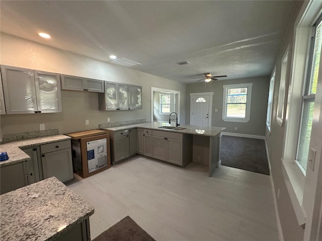 kitchen featuring gray cabinetry, light stone counters, ceiling fan, and sink