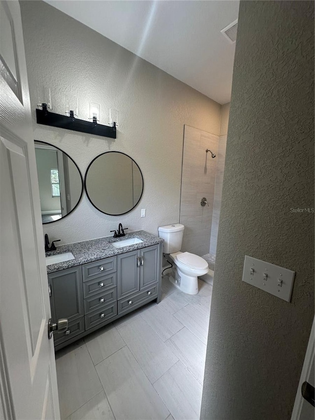 bathroom with toilet, tile flooring, dual vanity, and tiled shower