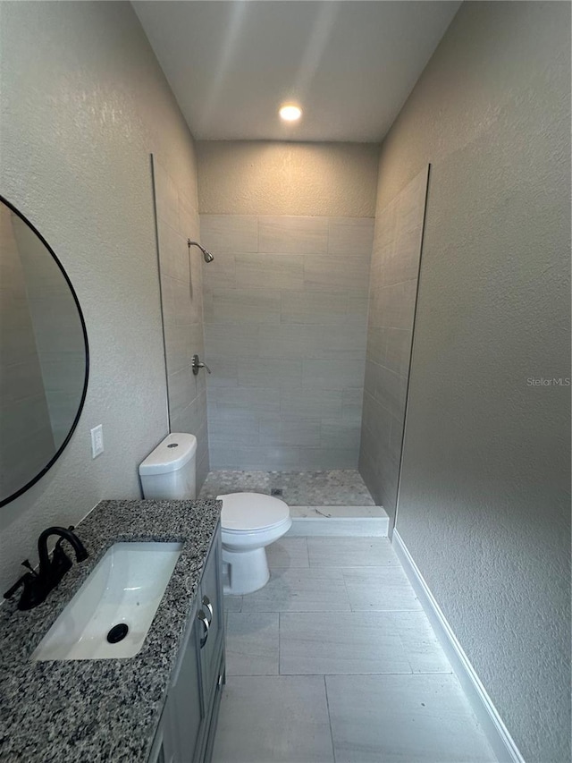 bathroom featuring tile floors, toilet, vanity, and tiled shower