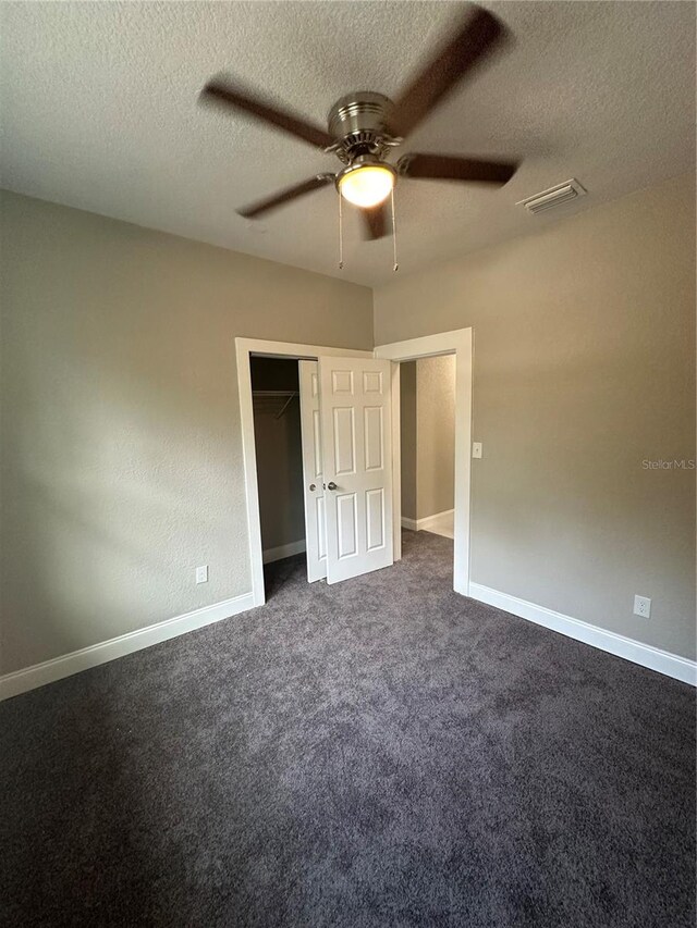 unfurnished bedroom with a closet, a textured ceiling, dark carpet, and ceiling fan