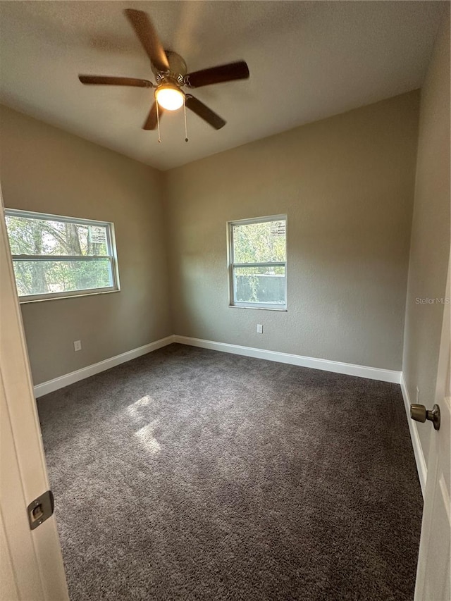 unfurnished room featuring plenty of natural light, dark colored carpet, and ceiling fan