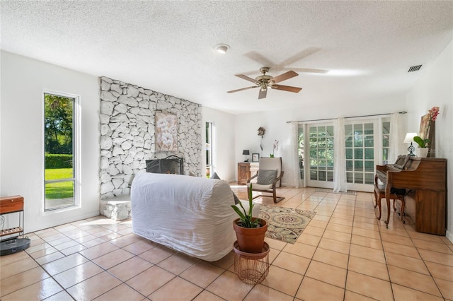 living room with ceiling fan, a textured ceiling, light tile patterned floors, and a stone fireplace