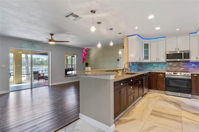 kitchen with kitchen peninsula, sink, decorative light fixtures, white cabinetry, and stainless steel appliances