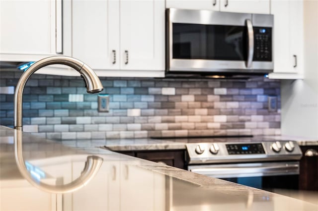 kitchen with light stone countertops, backsplash, white cabinetry, and appliances with stainless steel finishes