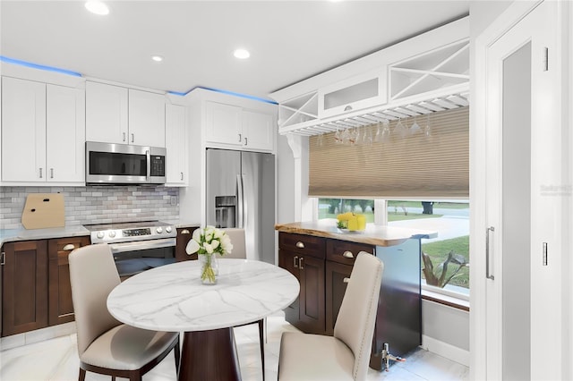 kitchen featuring white cabinets, decorative backsplash, dark brown cabinetry, and stainless steel appliances