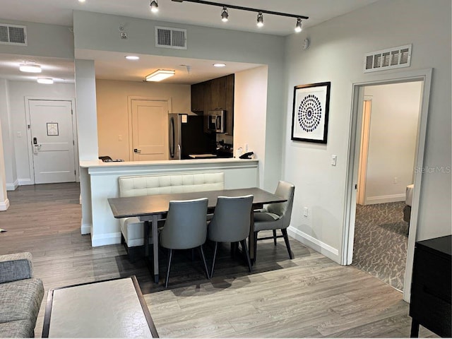 kitchen featuring rail lighting, stainless steel appliances, kitchen peninsula, hardwood / wood-style flooring, and dark brown cabinetry