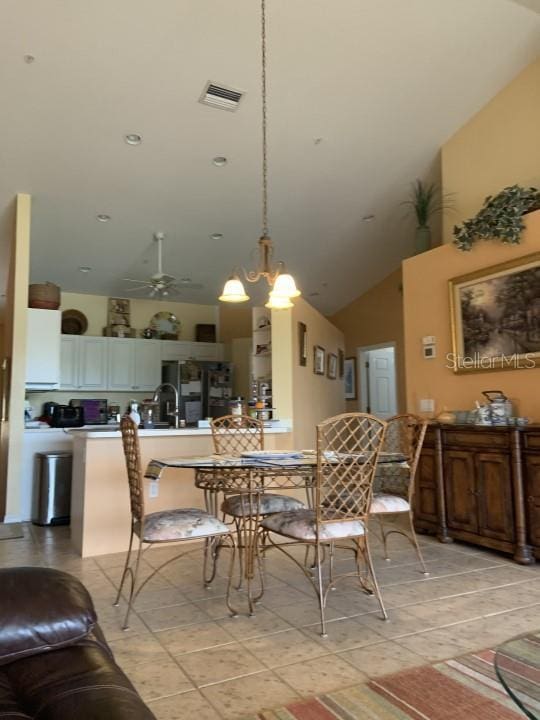 dining space featuring ceiling fan with notable chandelier, a towering ceiling, and sink