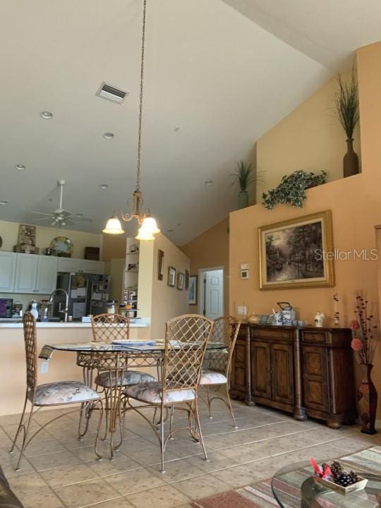 dining space featuring ceiling fan with notable chandelier, high vaulted ceiling, and sink