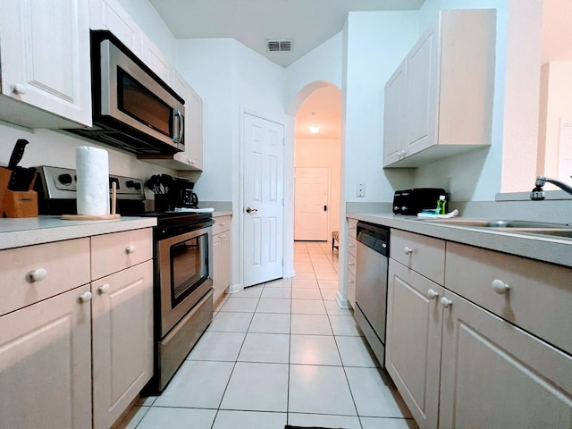 kitchen featuring appliances with stainless steel finishes, sink, light tile patterned floors, and white cabinets