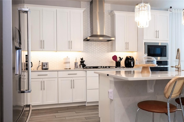 kitchen featuring white cabinets, decorative light fixtures, black microwave, and wall chimney range hood