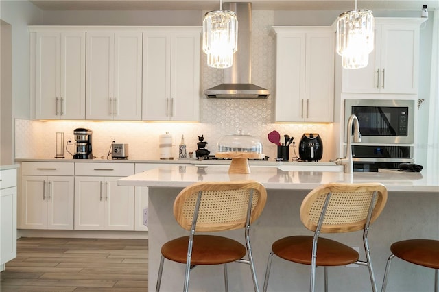 kitchen with wall oven, a breakfast bar area, wall chimney exhaust hood, and white cabinetry