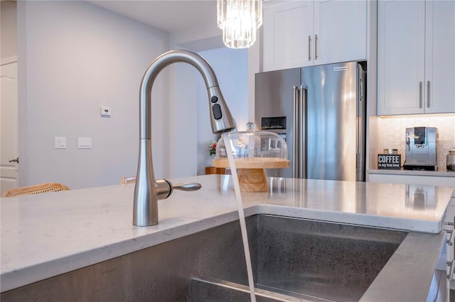 kitchen with hanging light fixtures, high quality fridge, white cabinets, light stone counters, and tasteful backsplash