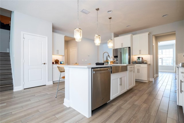 kitchen with a kitchen island with sink, hanging light fixtures, white cabinetry, and stainless steel appliances