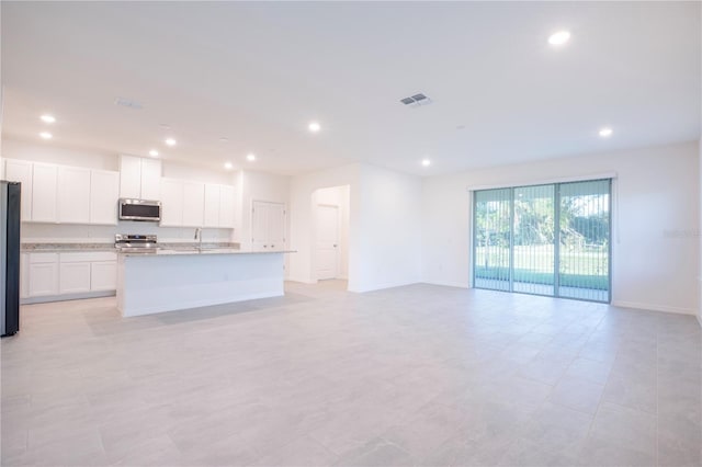 kitchen featuring appliances with stainless steel finishes, white cabinetry, an island with sink, sink, and light stone counters