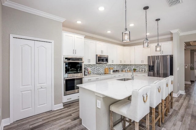 kitchen featuring a breakfast bar, sink, white cabinets, stainless steel appliances, and a center island with sink