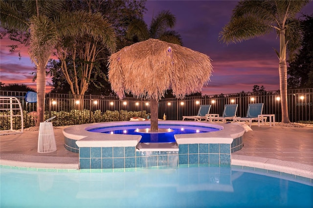 pool at dusk featuring pool water feature and a hot tub