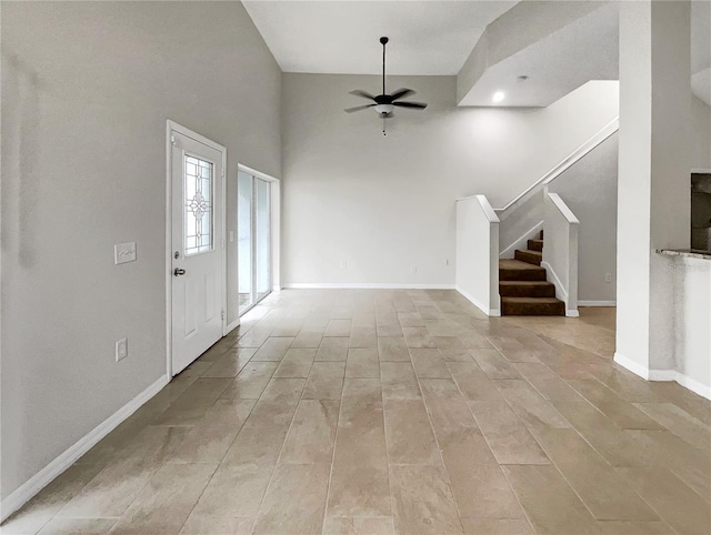 unfurnished living room featuring baseboards, ceiling fan, and stairs