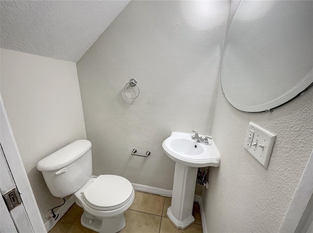 half bathroom featuring toilet, a sink, a textured ceiling, tile patterned flooring, and baseboards