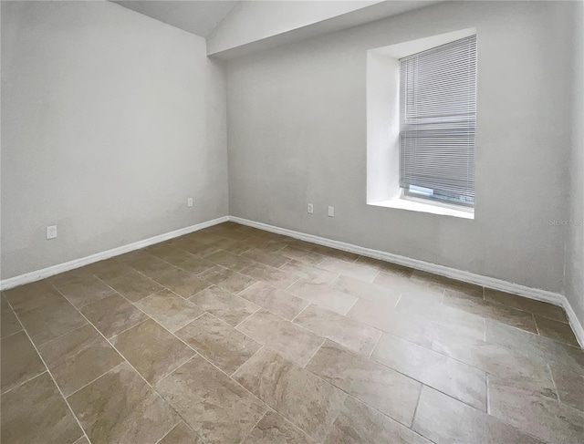 spare room featuring baseboards and vaulted ceiling