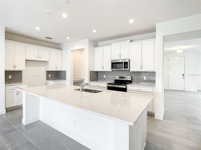 kitchen with backsplash, stainless steel appliances, sink, white cabinets, and an island with sink