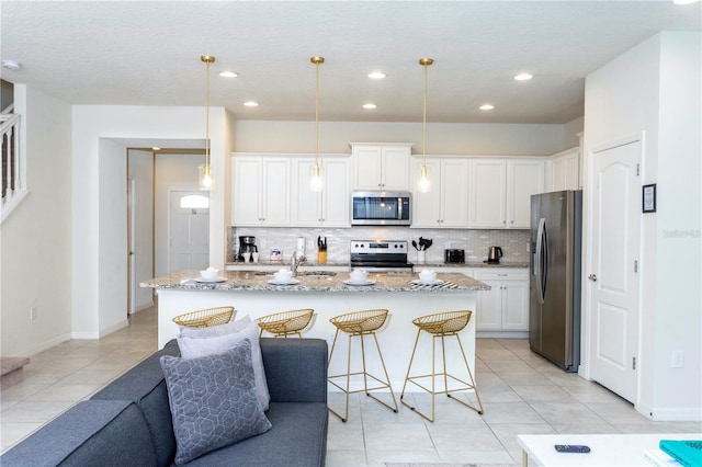 kitchen featuring decorative light fixtures, a center island with sink, stainless steel appliances, and white cabinets