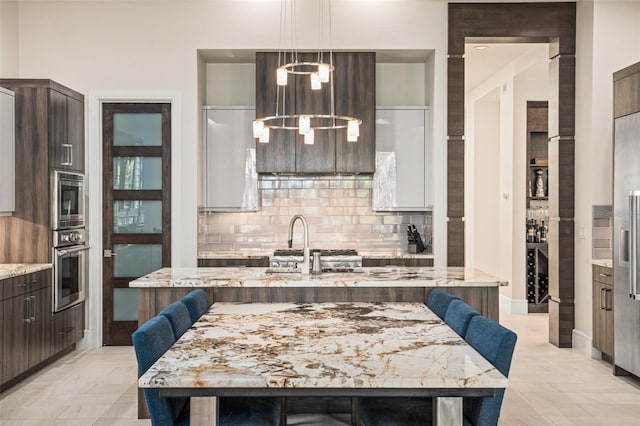 kitchen with dark brown cabinets, appliances with stainless steel finishes, a breakfast bar area, and an island with sink