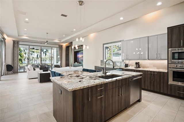 kitchen featuring a center island with sink, light stone counters, backsplash, sink, and stainless steel appliances