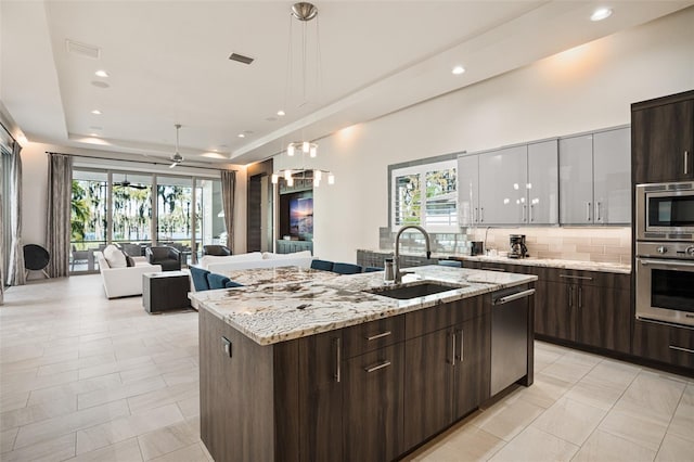 6109 Orta Ct, Windermere, FL 34786 - kitchen with a sink, appliances with stainless steel finishes, tasteful backsplash, a center island with sink, and a raised ceiling