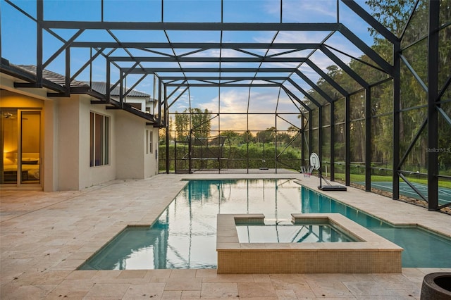 pool at dusk featuring an in ground hot tub, a patio, and glass enclosure