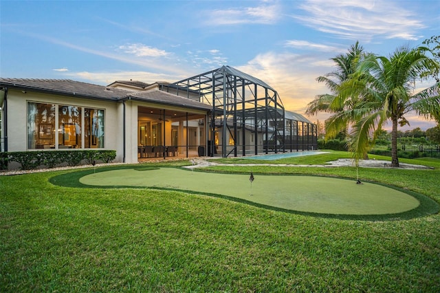 back house at dusk featuring a patio, a lawn, and glass enclosure