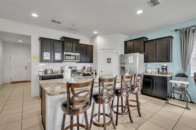 kitchen featuring light tile patterned flooring, a kitchen breakfast bar, stainless steel appliances, and an island with sink