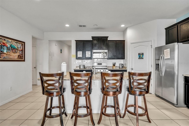 kitchen with light stone counters, light tile patterned floors, appliances with stainless steel finishes, and a kitchen island with sink