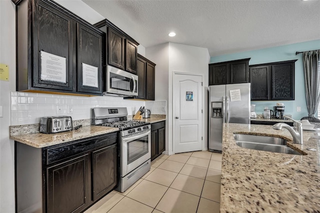 kitchen with light tile patterned floors, stainless steel appliances, light stone countertops, a textured ceiling, and sink