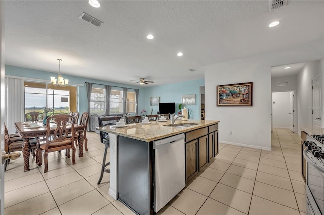 kitchen with appliances with stainless steel finishes, decorative light fixtures, sink, a kitchen island with sink, and light stone counters