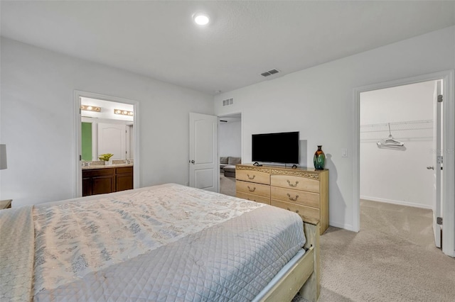 bedroom featuring a spacious closet, light colored carpet, a closet, and ensuite bath