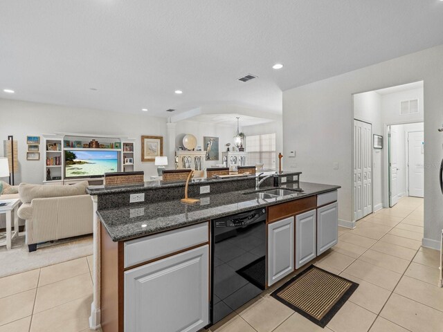kitchen featuring dishwasher, sink, dark stone countertops, light tile patterned floors, and an island with sink