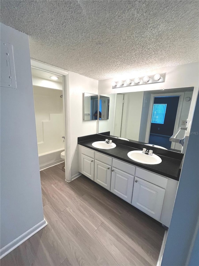 full bathroom with hardwood / wood-style floors, vanity, toilet, a textured ceiling, and washtub / shower combination