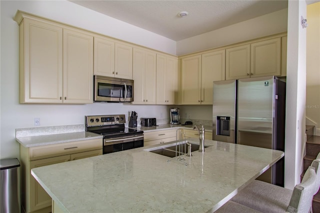 kitchen featuring stainless steel appliances, an island with sink, cream cabinets, and sink