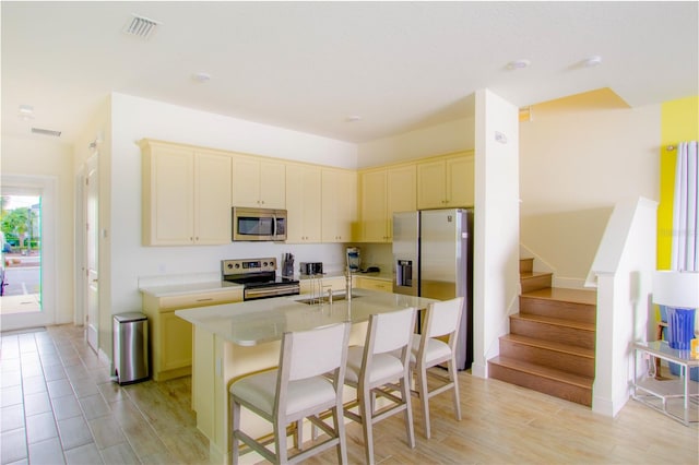 kitchen with a kitchen island with sink, sink, stainless steel appliances, and a breakfast bar