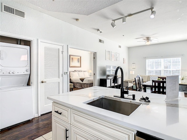 kitchen featuring a textured ceiling, stacked washing maching and dryer, ceiling fan, dark hardwood / wood-style floors, and sink