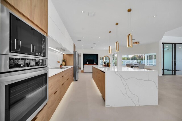 kitchen featuring black electric stovetop, light stone counters, white cabinets, hanging light fixtures, and a spacious island