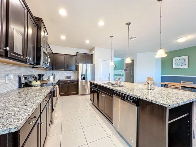 kitchen with stainless steel appliances, dark brown cabinets, a center island with sink, and decorative light fixtures