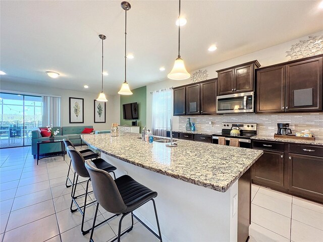 kitchen with stainless steel appliances, light tile flooring, hanging light fixtures, sink, and a kitchen island with sink