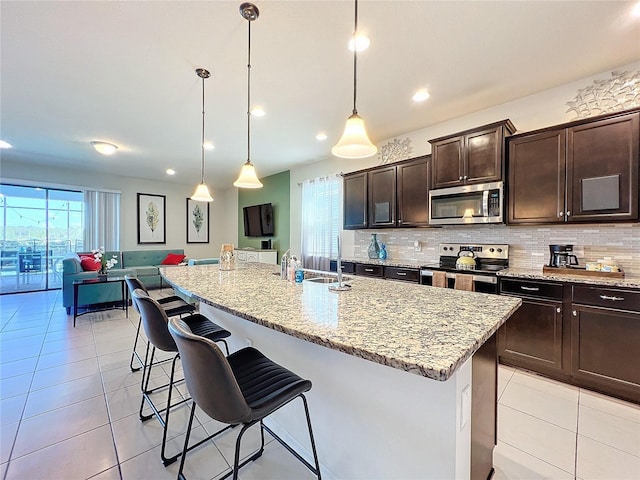 kitchen with decorative light fixtures, an island with sink, and appliances with stainless steel finishes