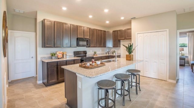 kitchen with sink, a kitchen island with sink, black appliances, light stone countertops, and a kitchen bar