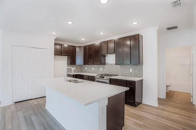 kitchen featuring stainless steel range with gas stovetop, sink, a center island with sink, and light wood-type flooring